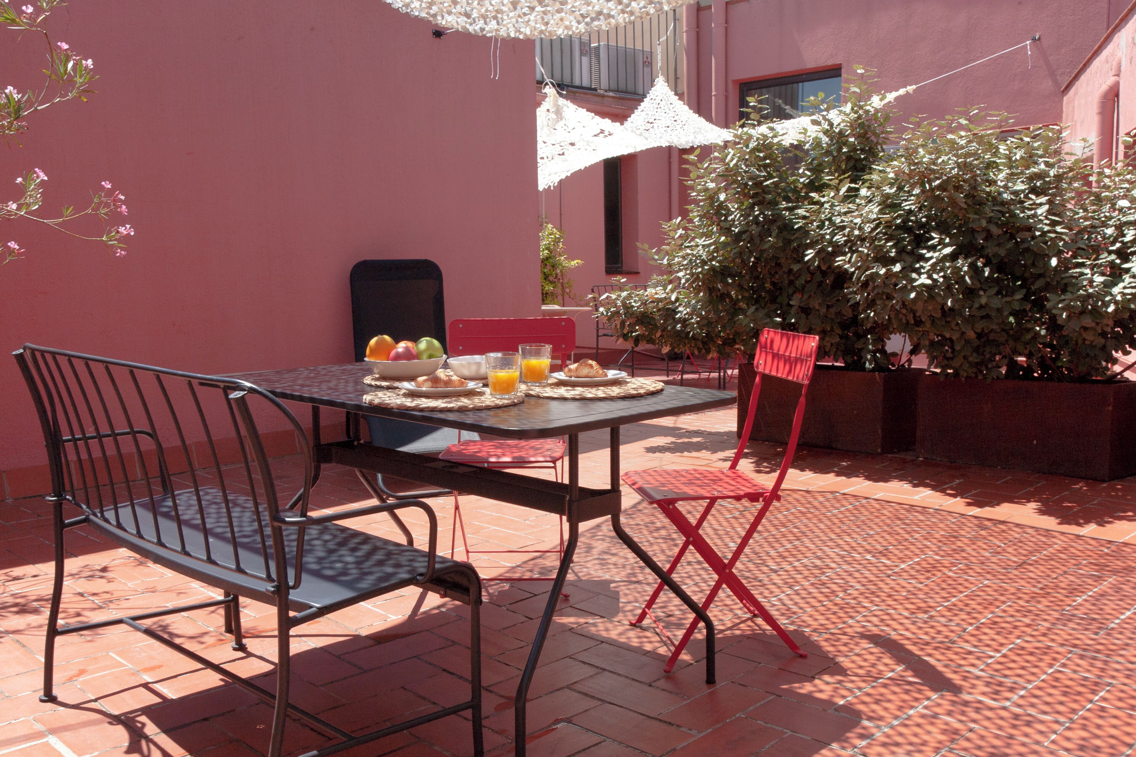 An outdoor patio with a table set for breakfast, including fruits, bread, and juice.