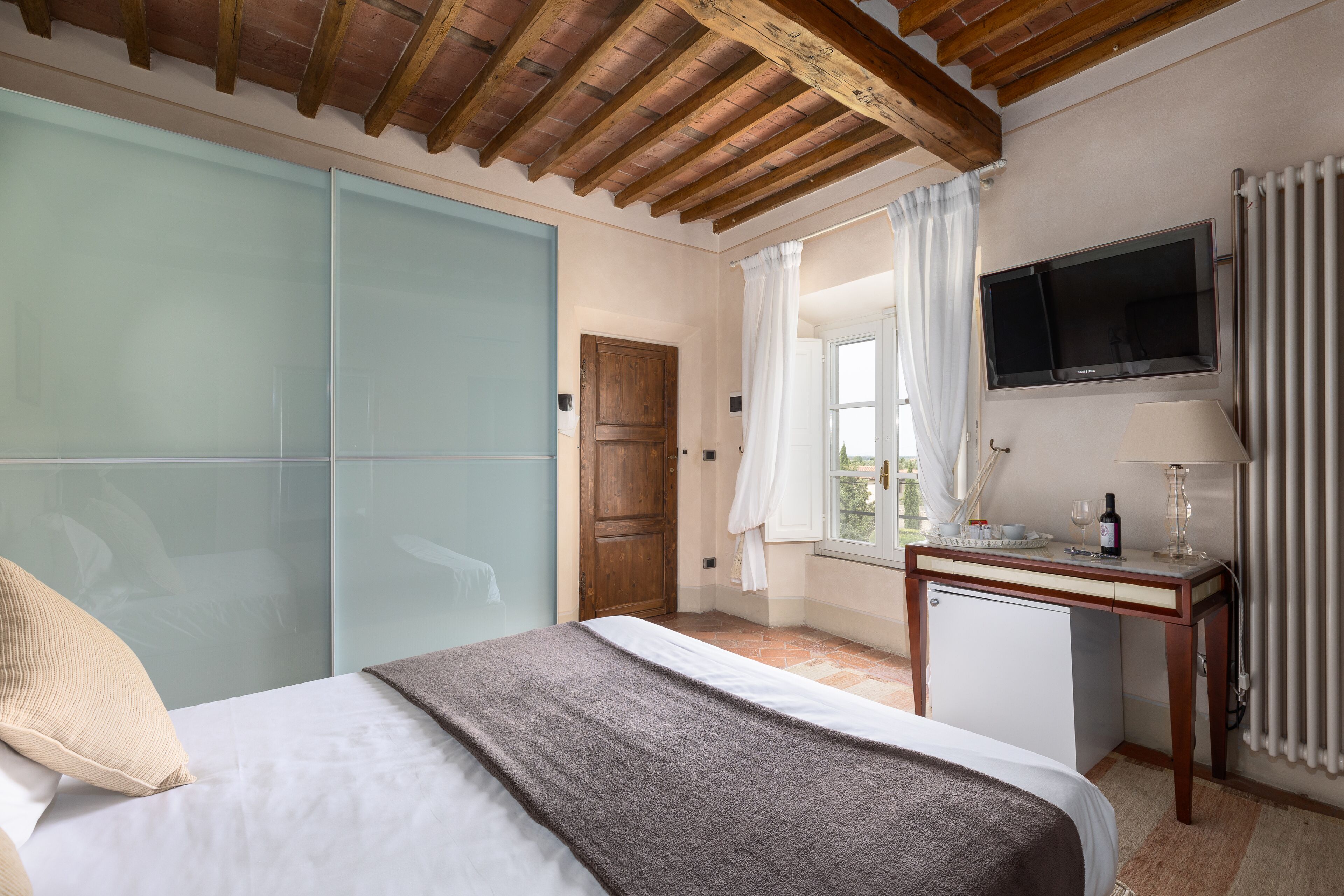 Een hotelkamer met een bed, een bureau, een televisie en een raam met gordijnen.