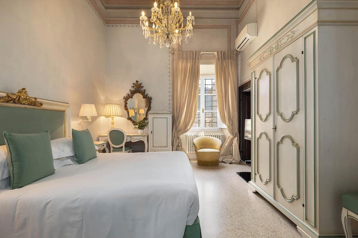 Une chambre spacieuse avec un grand lit, un lustre, une coiffeuse avec un miroir et une armoire.