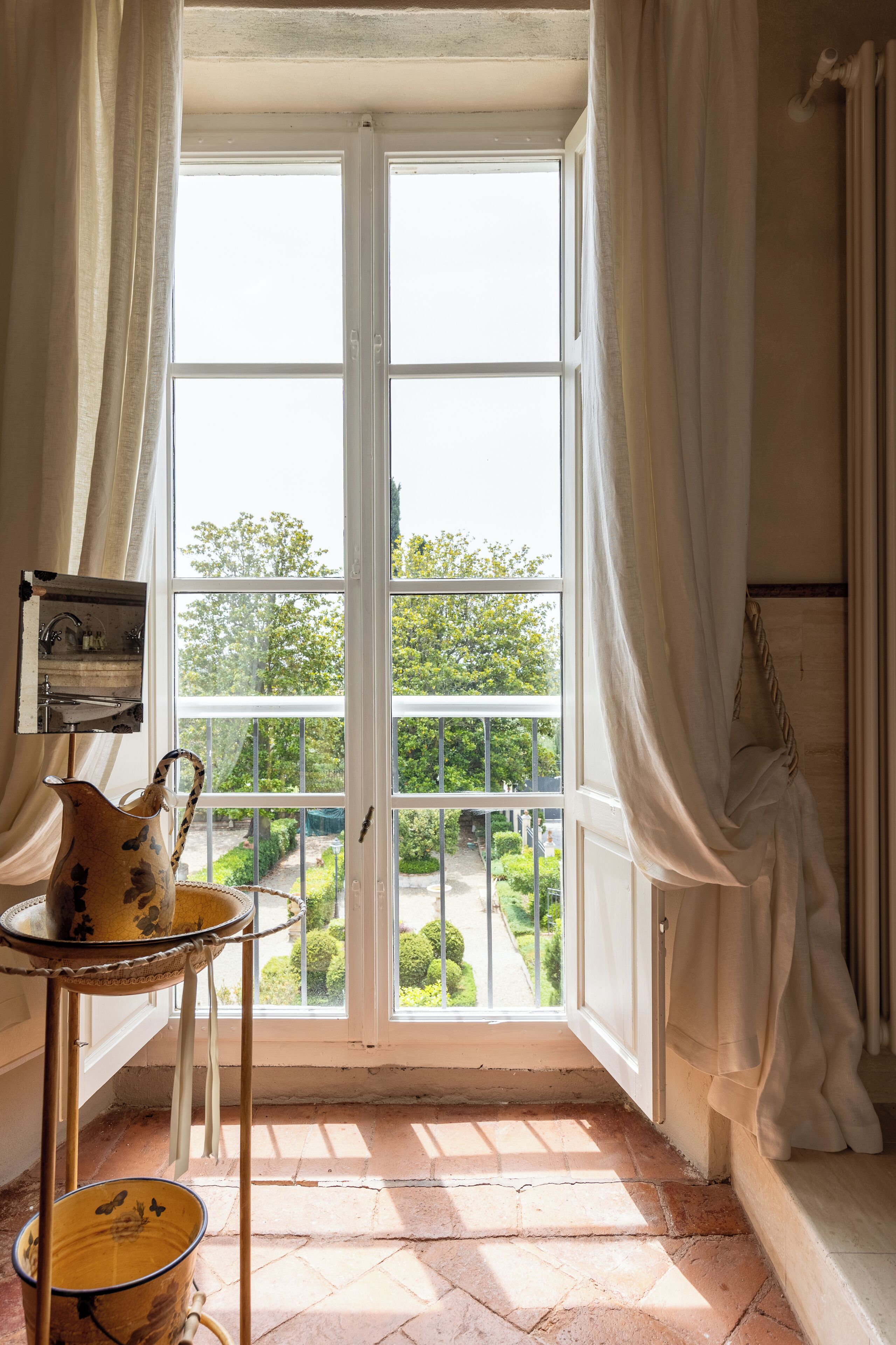 A room with a large window, a small table with a pitcher, and a view of greenery outside.
