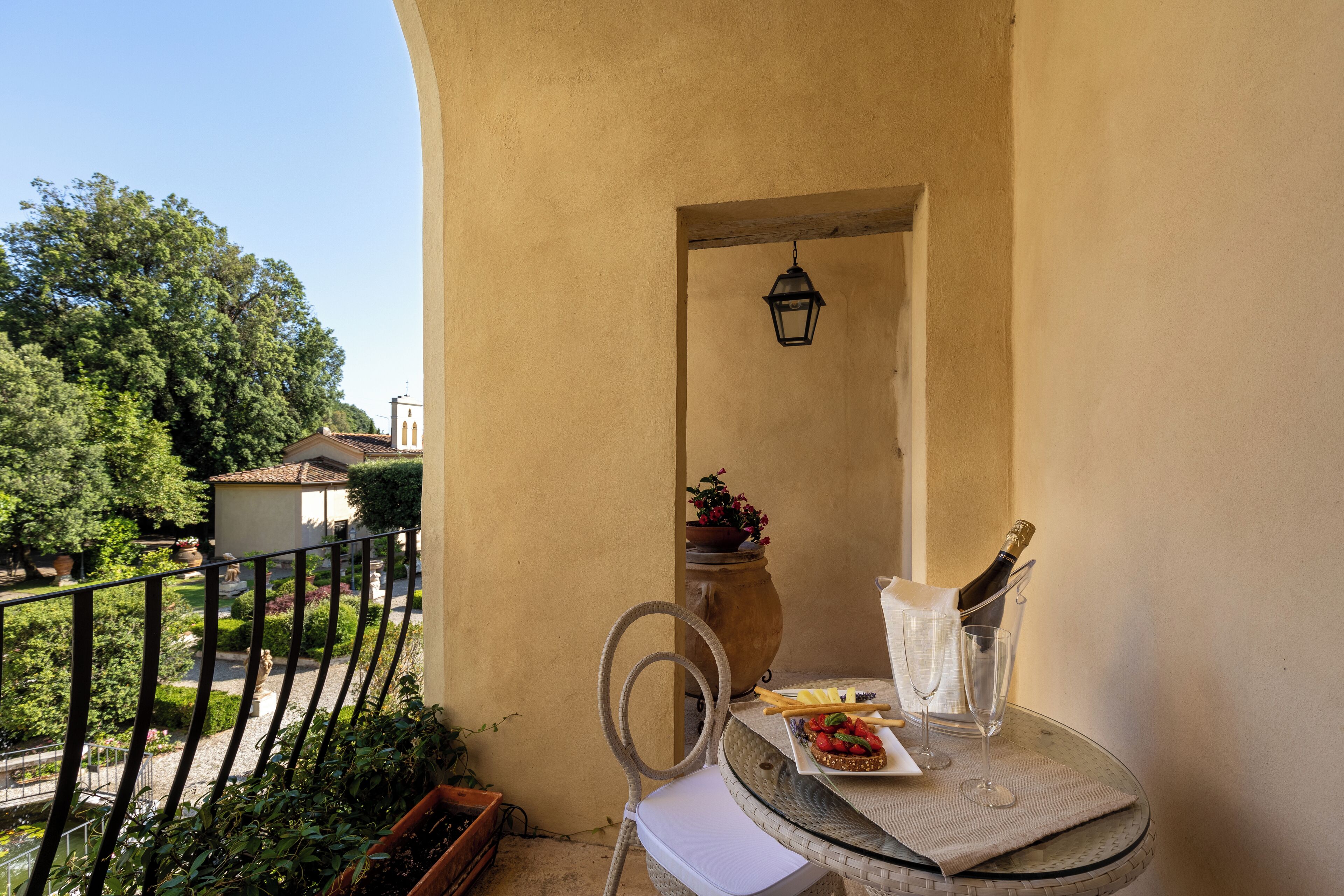 A balcony with a table set for a meal, a potted plant, and a bottle of champagne.