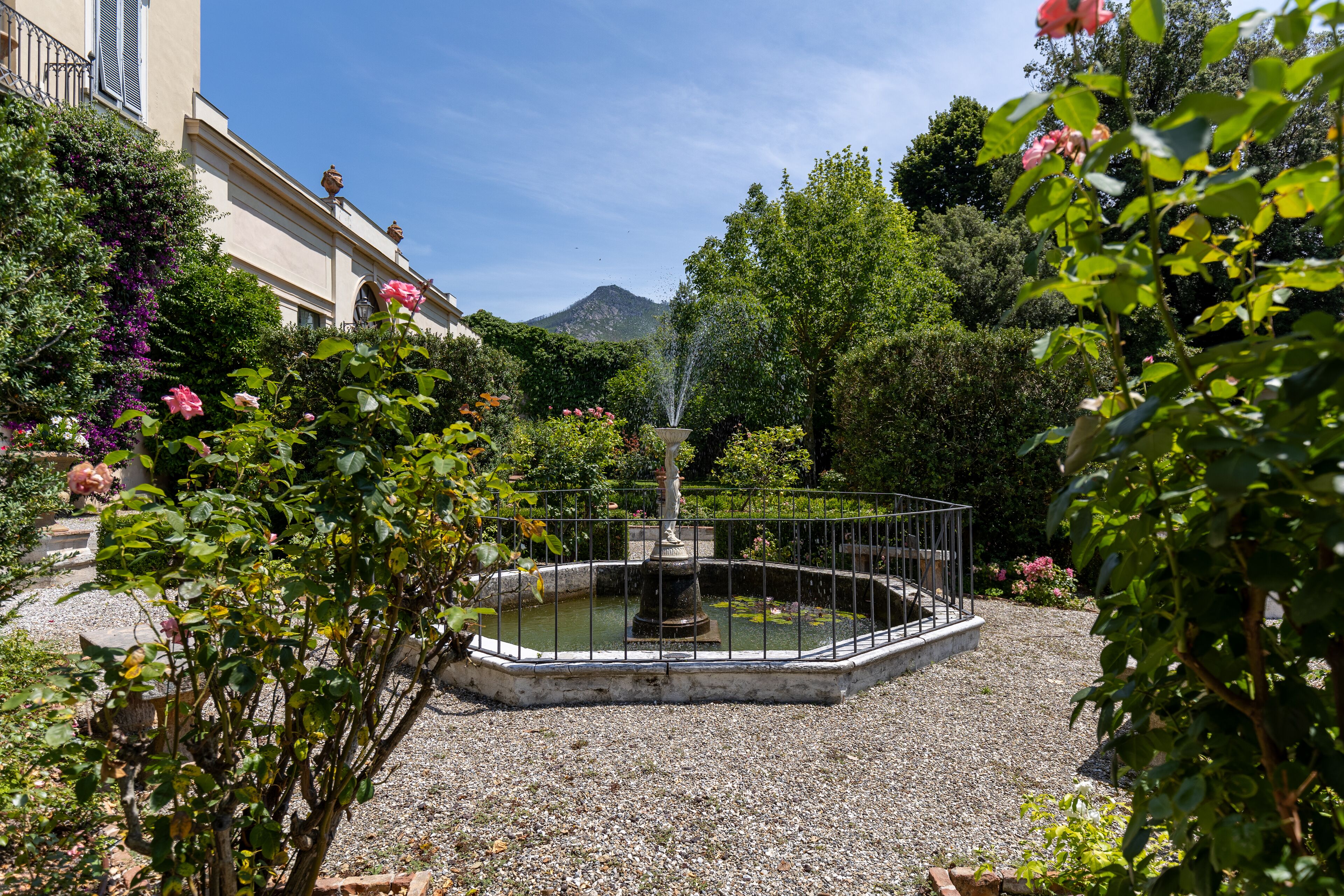 Um jardim com uma fonte, rodeado por cascalho e diversas plantas.