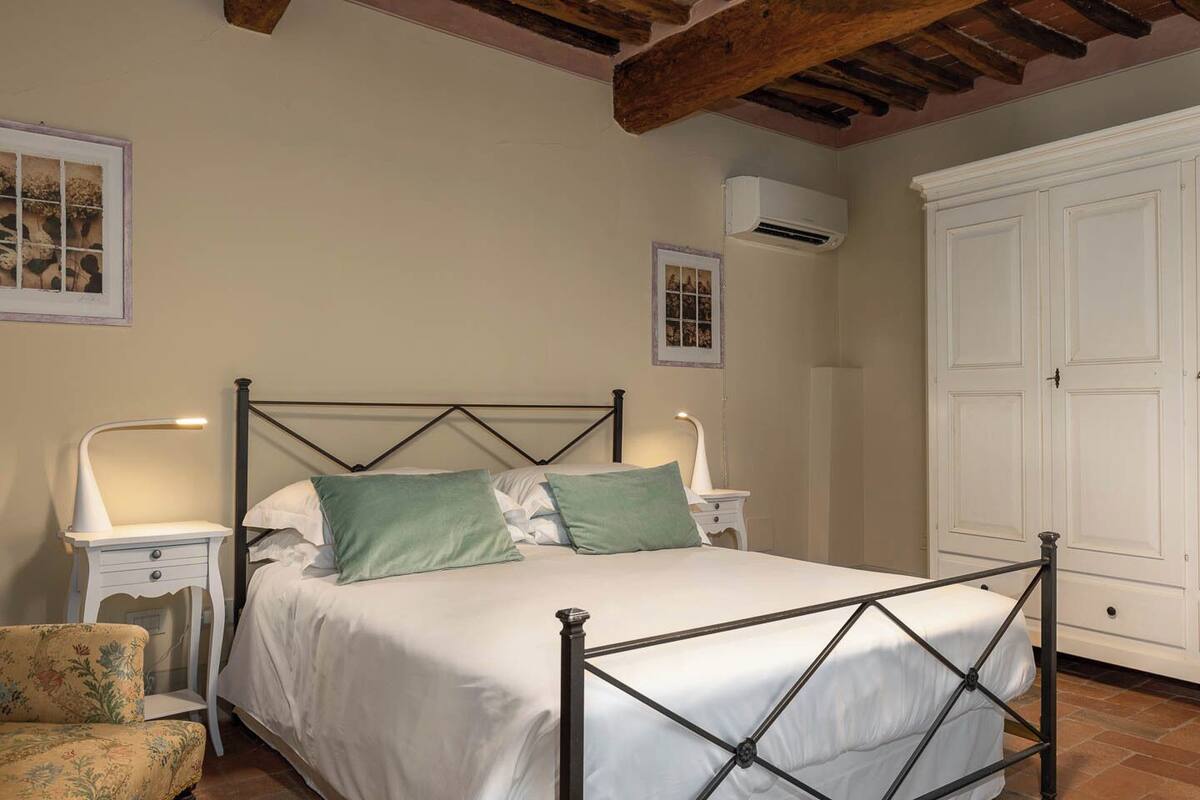 Une chambre à coucher comprenant un lit, des tables de chevet, une chaise, une armoire et un appareil de climatisation.