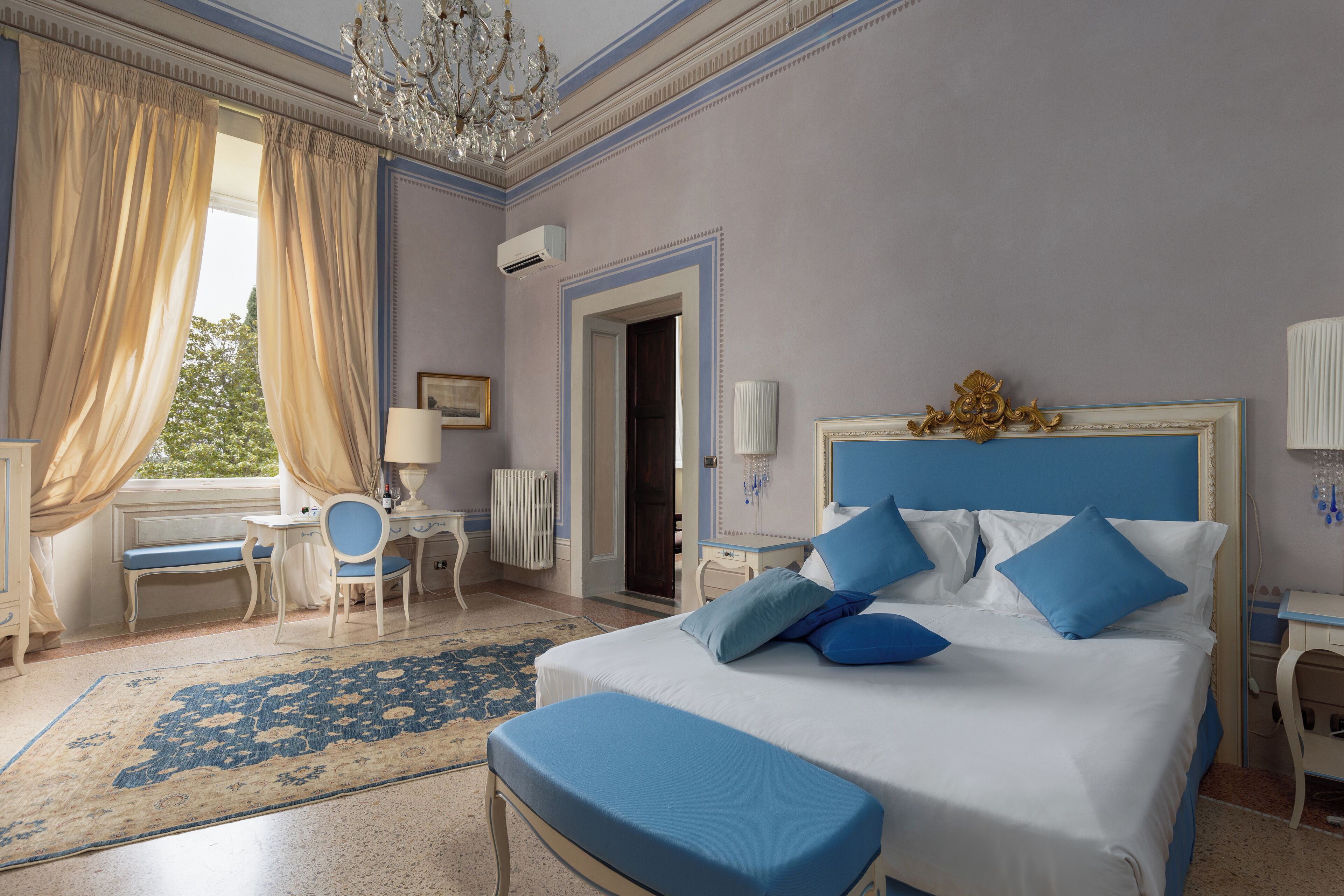 A bedroom with a large bed, a desk, a chair, and a window with curtains.