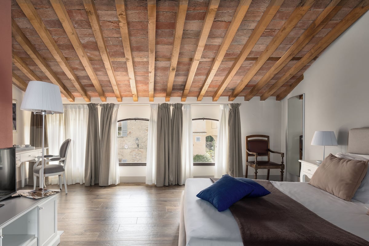 Une chambre d’hôtel avec un plafond en bois, un lit avec un oreiller bleu, un bureau avec une lampe et une chaise.
