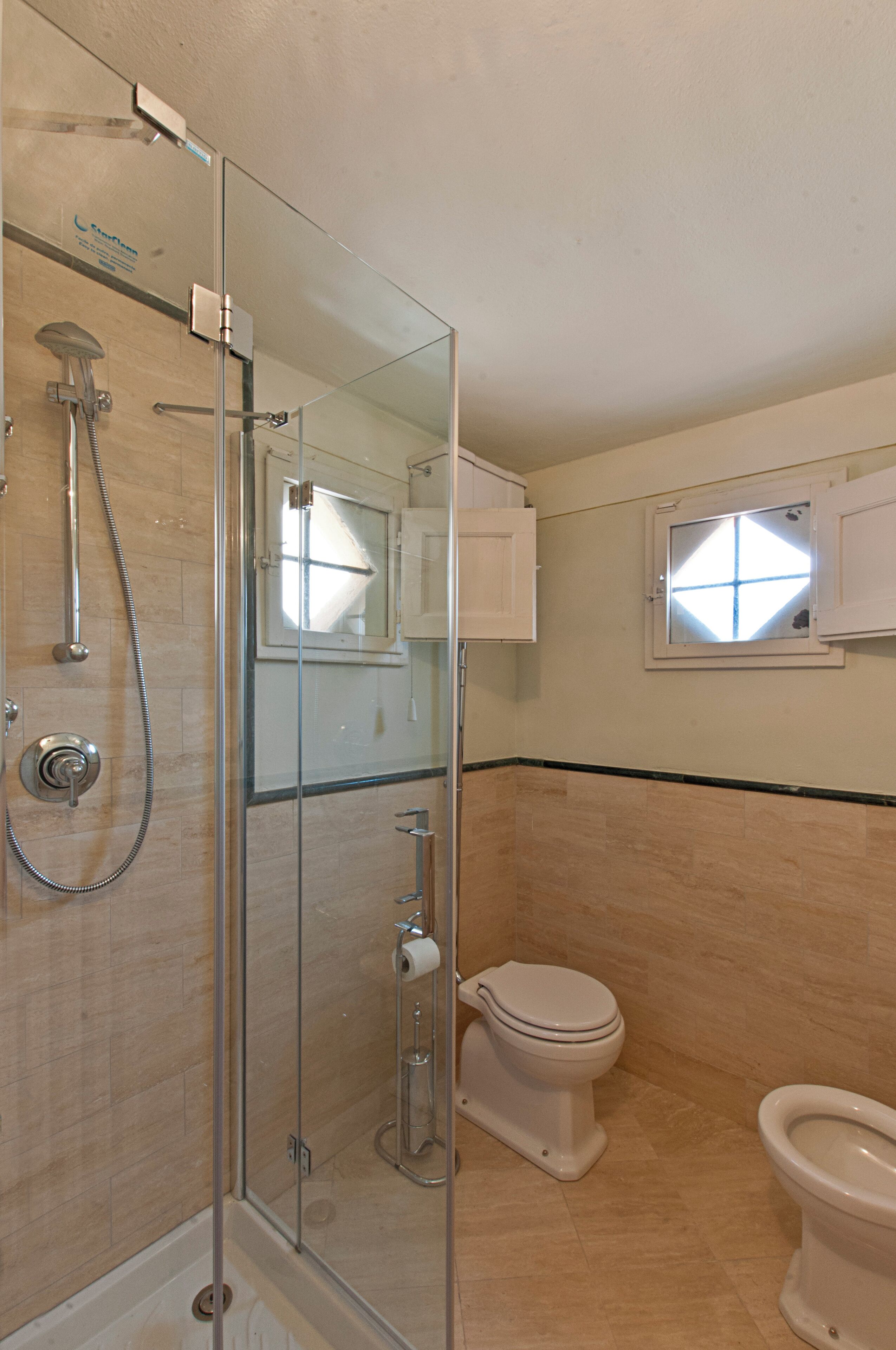 Un baño con ducha de vidrio, inodoro y un ventanal pequeño.