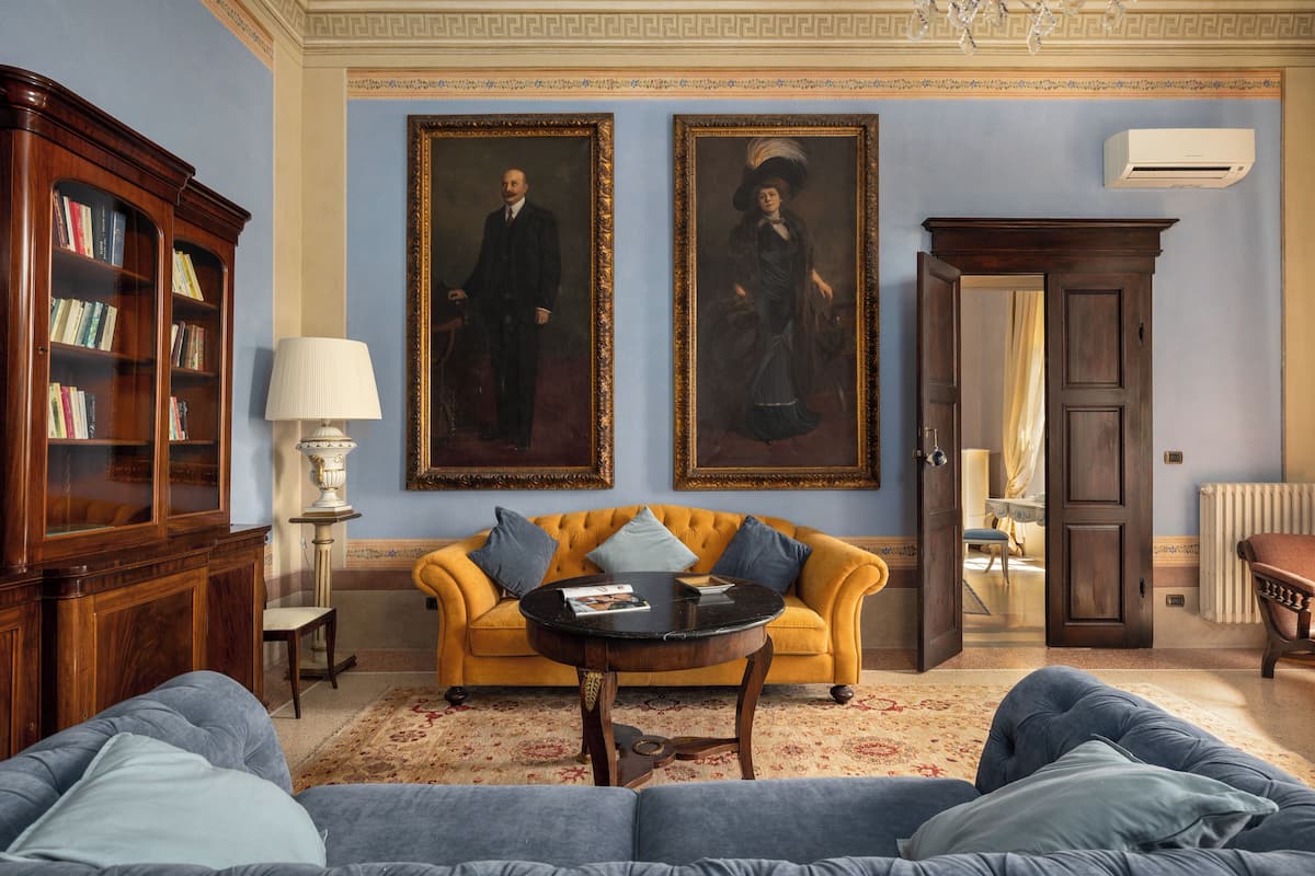 Une pièce avec un canapé jaune, une table basse ronde, une bibliothèque et deux portraits encadrés accrochés au mur.