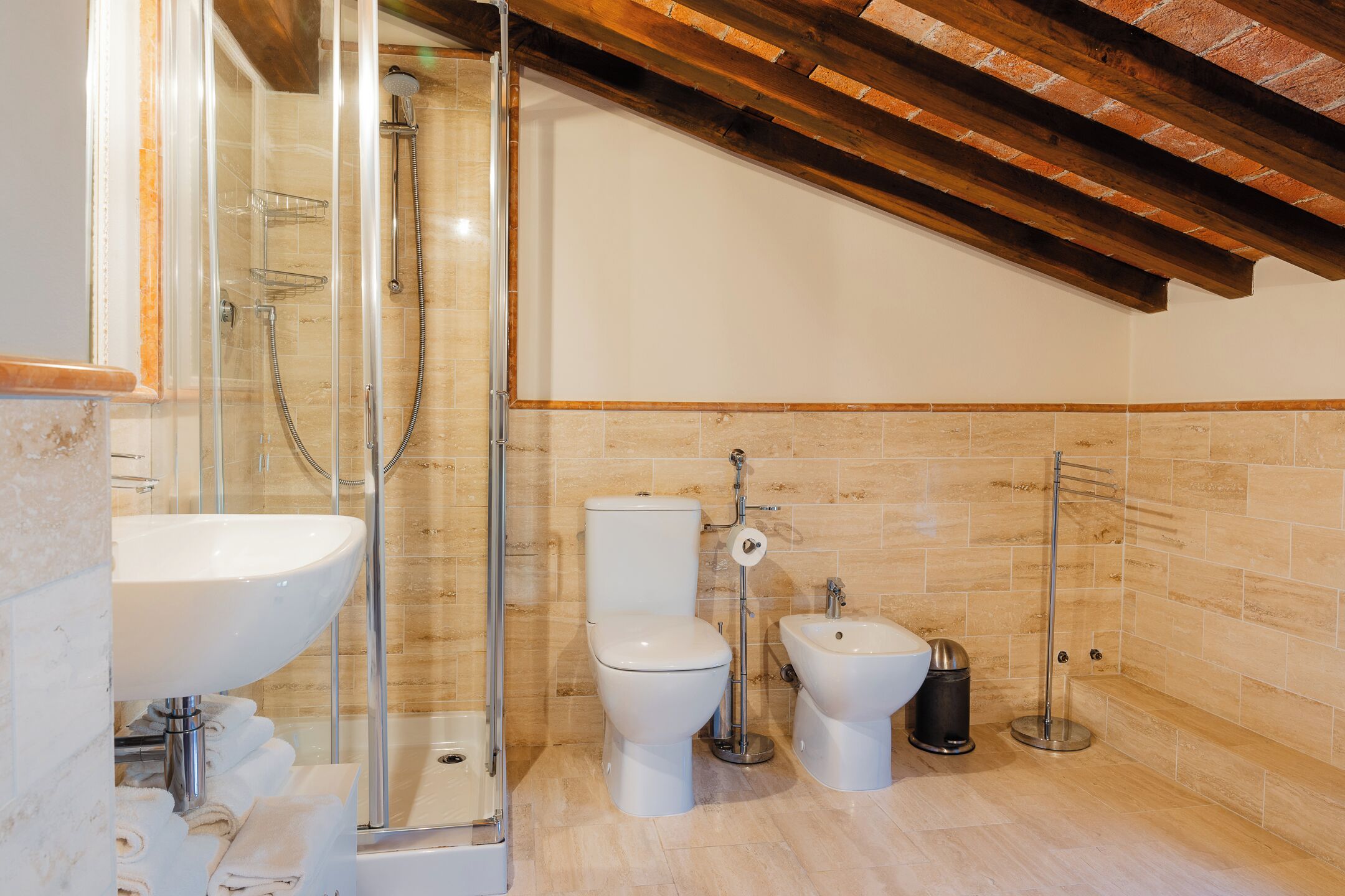 A bathroom with a glass-enclosed shower, a white sink, a toilet, and a bidet.