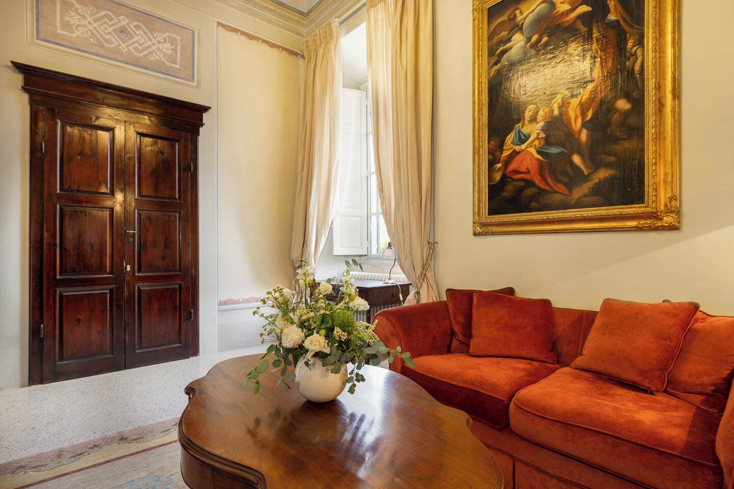 A room with a wooden cabinet, a red sofa, a vase of flowers, and a painting on the wall.