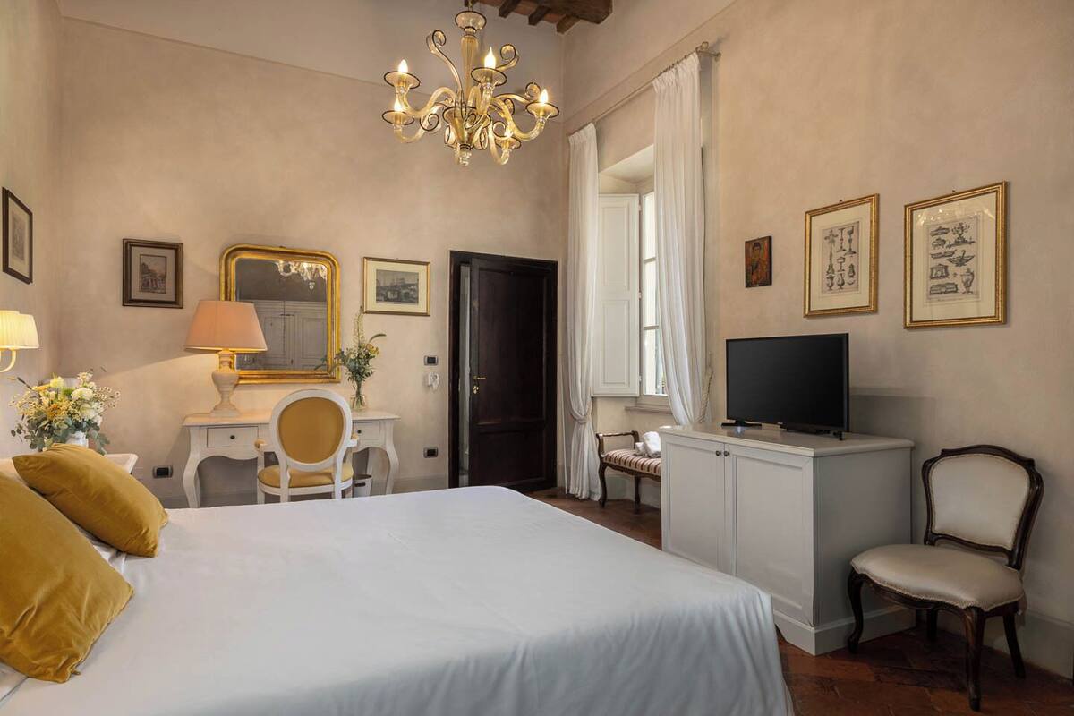 Une chambre d’hôtel avec un grand lit, un bureau avec une chaise, une télévision et un lustre.