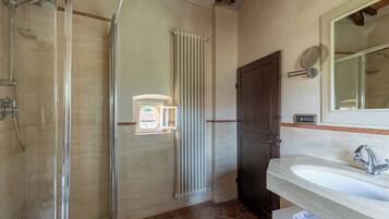 A bathroom with a glass-enclosed shower, a white sink, and a wooden door.