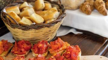 A basket of bread rolls, a wooden cutting board with tomato slices, and a wooden-handled knife.