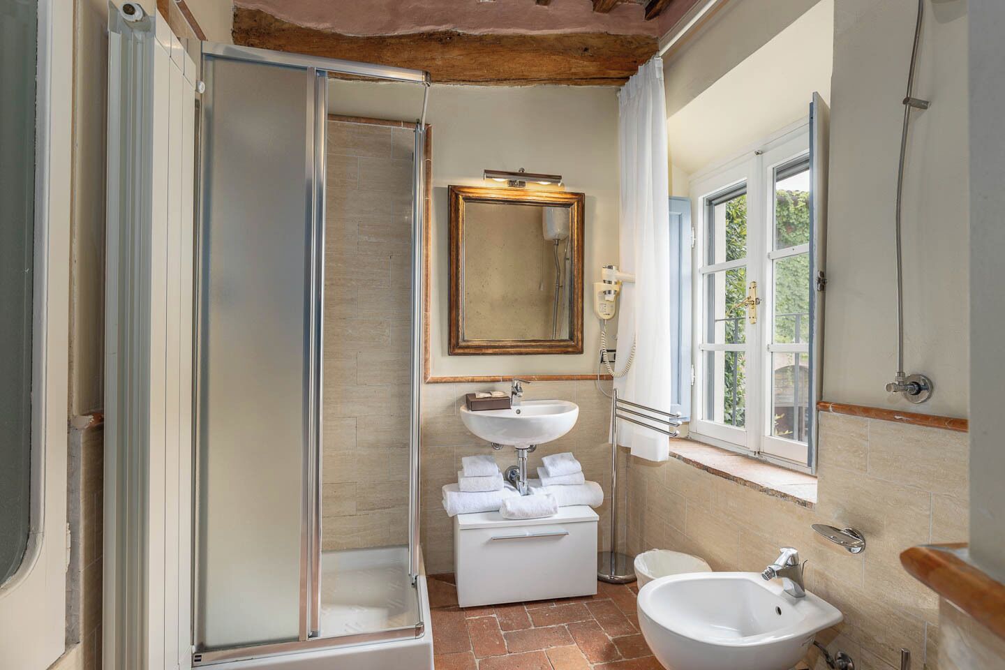 Un baño con cabina de ducha de vidrio, lavamanos, espejo y ventana.