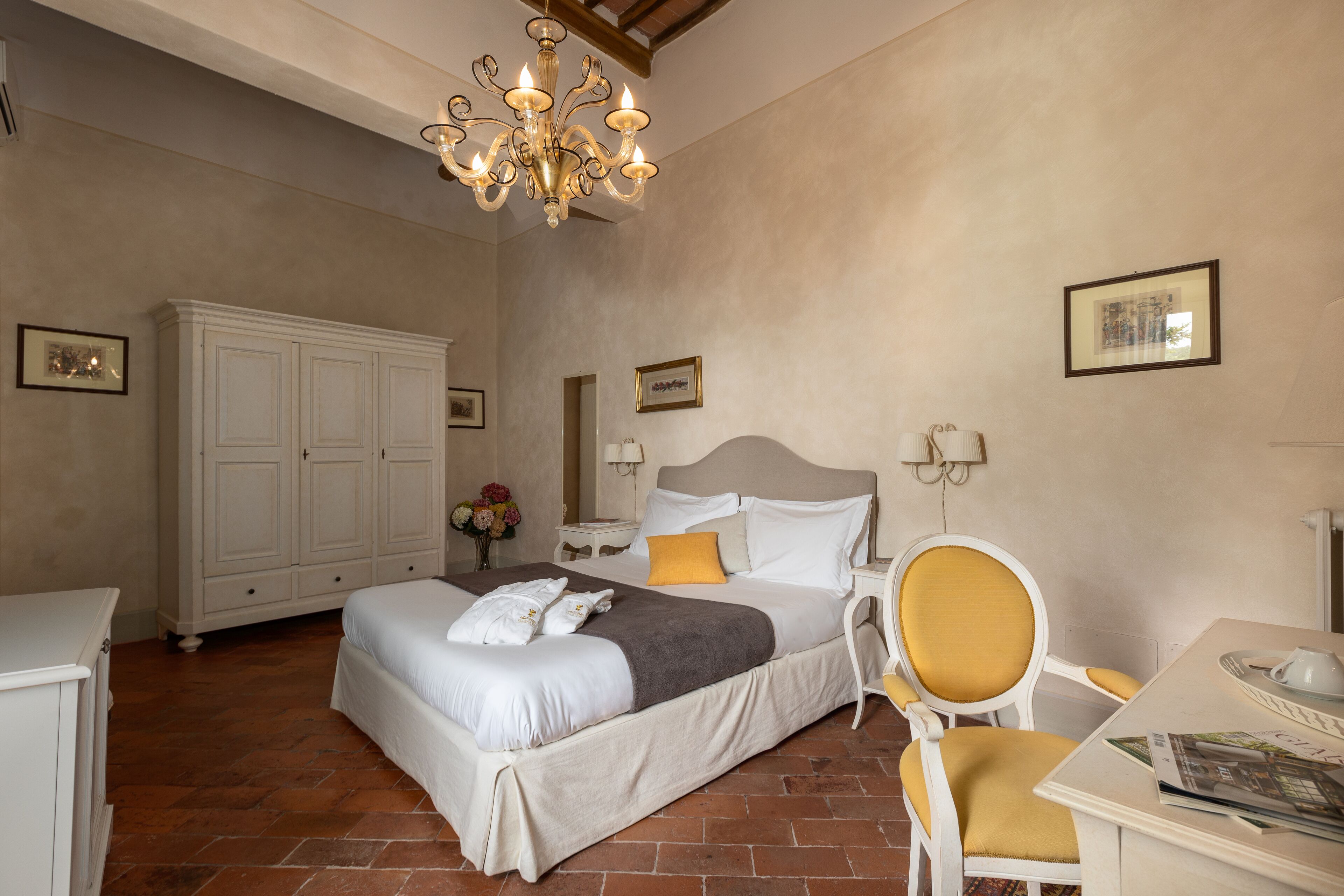 Une chambre à coucher avec un grand lit, une armoire, une chaise, une table et un lustre.