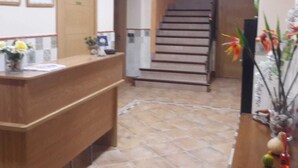 Una zona de recepció amb un taulell de fusta, una escala i un paviment de rajoles.