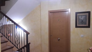 Un passadís amb una porta de fusta marcada amb el número 2, una escala amb barana decorativa i una obra d'art floral emmarcada a la paret.