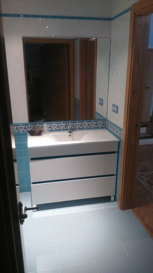 Un baño con un lavamanos blanco, paredes con azulejos azules y una puerta de madera.