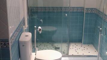 Een badkamer met toilet, douchecabine en blauwe betegelde wanden.