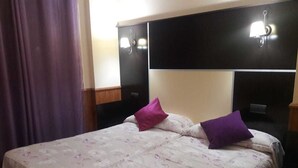 Habitació d'hotel amb un llit, dos almoinos, una tauleta de nit i una làmpada penjada a la paret.