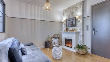 A modern living room with a grey sofa, a fireplace, a large mirror, and a door.