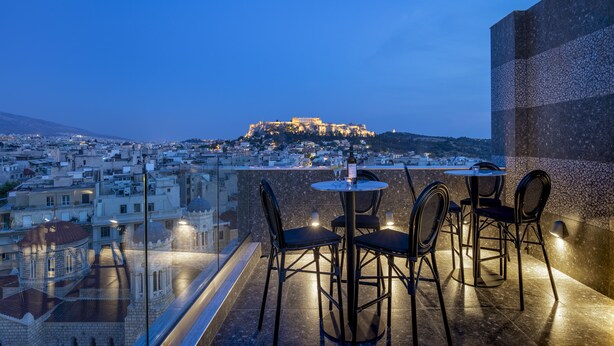 Terraza en la azotea con vistas a una antigua fortaleza en la colina, amueblada con mesas y sillas redondas, dominando un paisaje urbano.