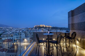 Terraza en la azotea con vistas a una antigua fortaleza en la colina, amueblada con mesas y sillas redondas, dominando un paisaje urbano.