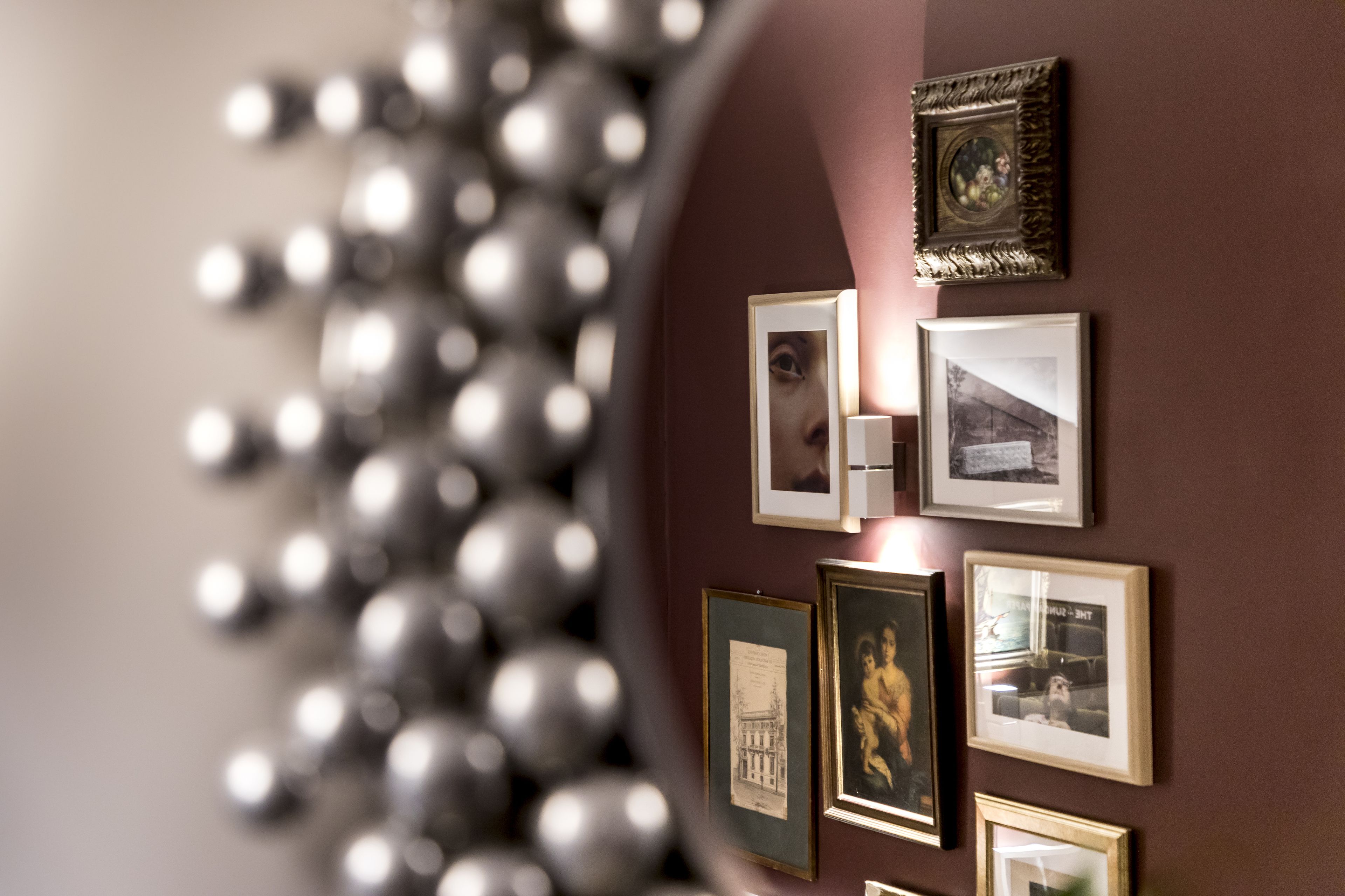 Una parete con diverse fotografie incorniciate e uno specchio decorativo.