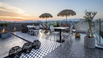 A rooftop terrace with outdoor seating, thatched umbrellas, and a checkered floor.