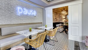 Un café moderno con un letrero de neón que dice 'pause', bancos de madera, sillas de mimbre y un suelo estampado.