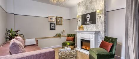 A modern living room with a fireplace, a green armchair, a pink sofa, and a round coffee table.