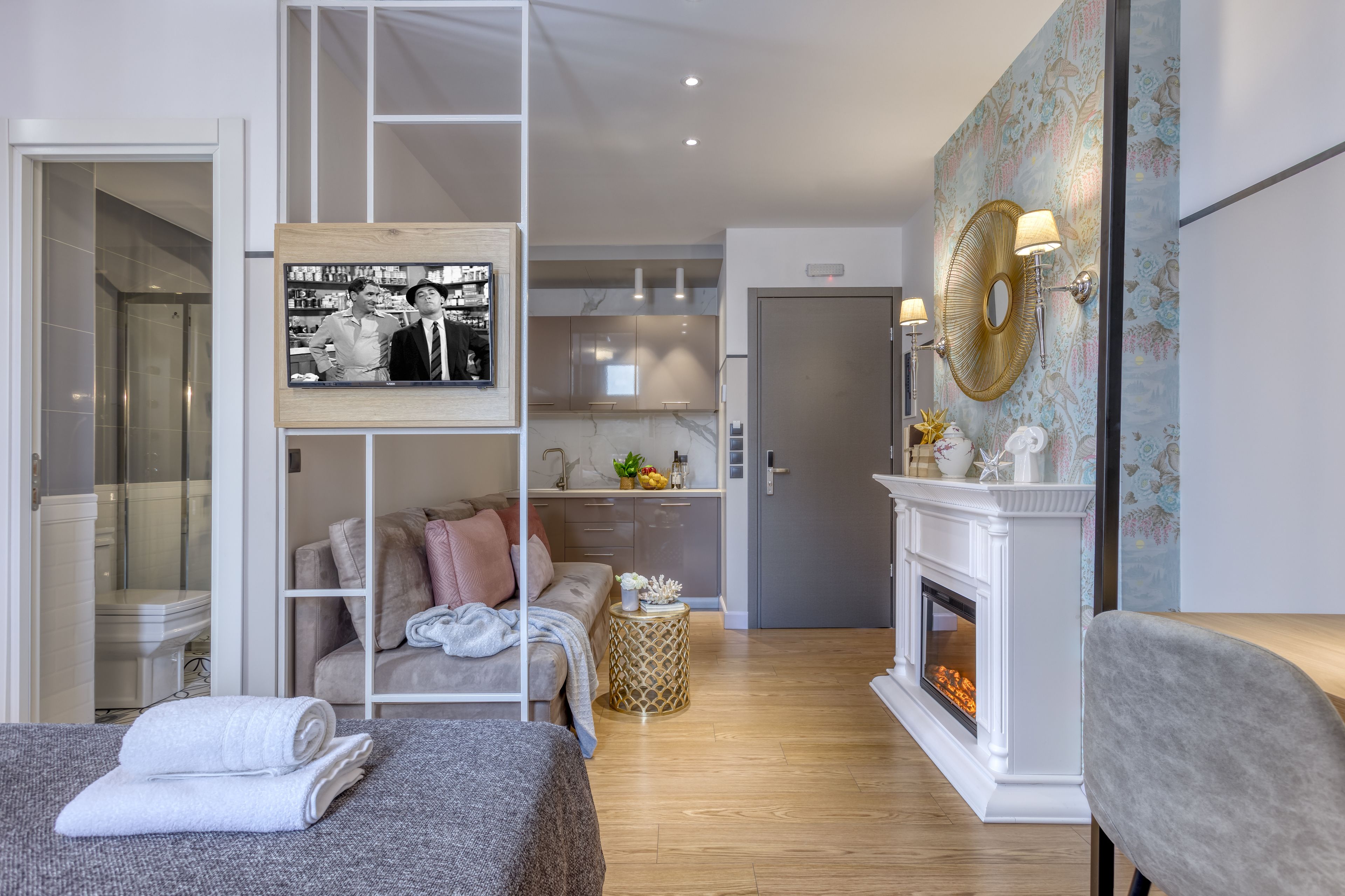 A modern hotel room with a sofa, a small round table, a fireplace, and a wall-mounted mirror.