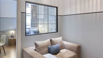 A modern living room with a beige sofa, a white ottoman, and a geometric-patterned window.