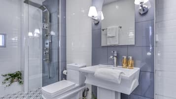 A modern bathroom with a glass shower enclosure, a white toilet, a sink with a towel, and a mirror with wall-mounted lights.