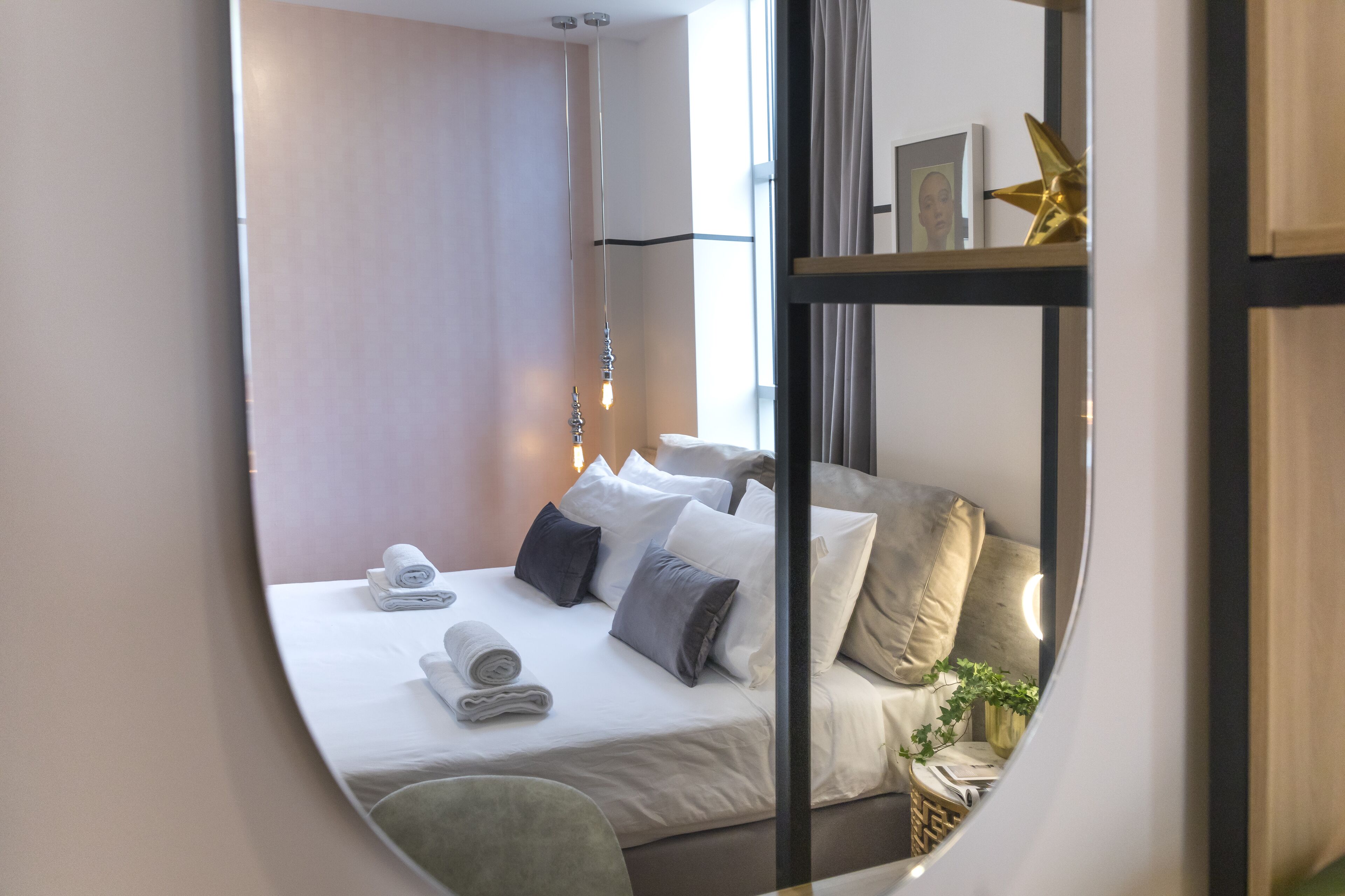 Quarto de hotel com cama, almofadas, mesa de cabeceira, abajur e janela.