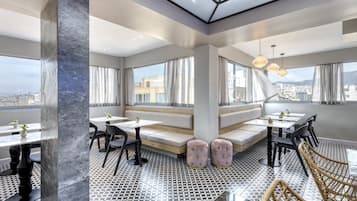Um restaurante moderno com tetos altos, grandes janelas e uma variedade de opções de assento, incluindo mesas, bancos e banquinhos estofados.