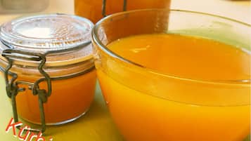 A glass bowl of orange marmalade with metal containers in the background.