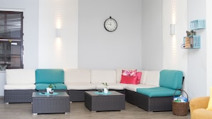 A modern living room with a sectional sofa, two side tables, a wall clock, and decorative wall sconces. - Hotel zum Schwan (Beeskow)