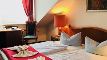 A hotel room with two beds, a desk, a chair, a lamp, and a painting on the wall.