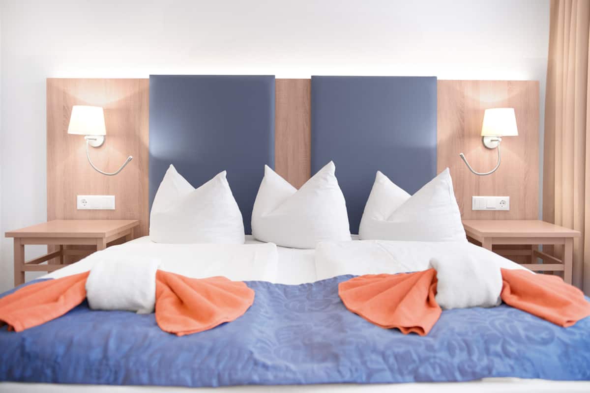 A hotel room with a large bed, two bedside tables, and a headboard with two wall-mounted lamps.