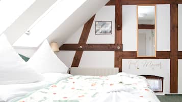 Un dormitorio con techo inclinado, una cama con ropa de cama floral, una mesita de noche, un espejo y una pared con un cartel que dice 'Just Married'.