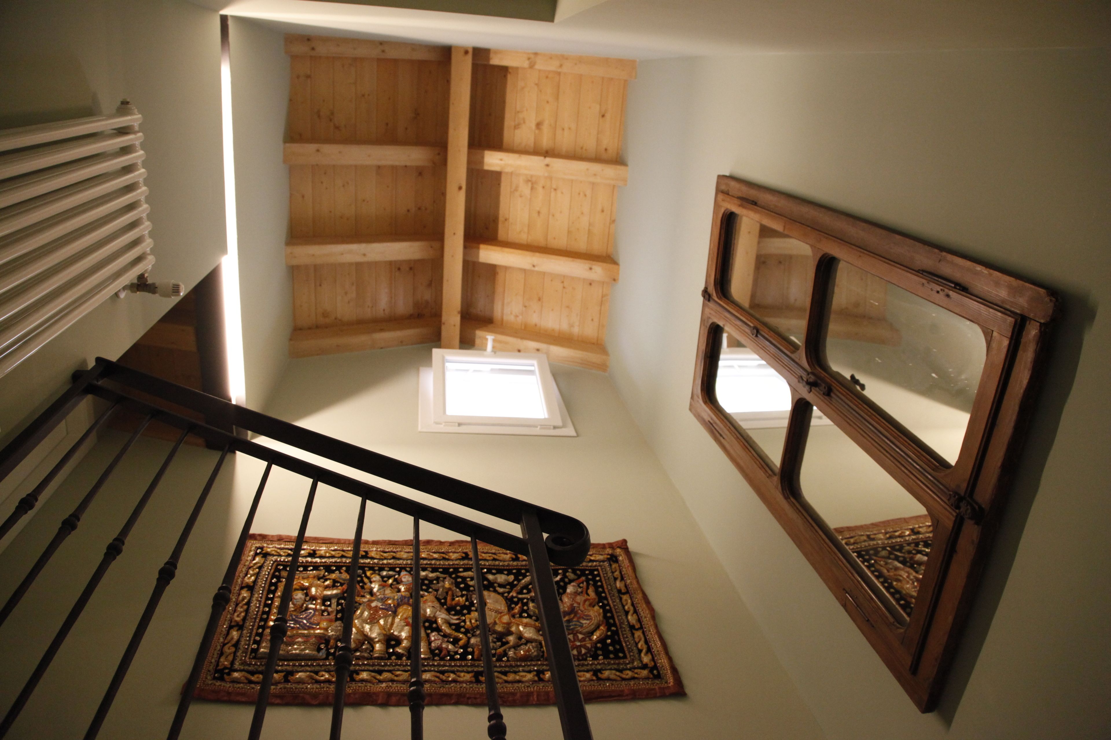 A wooden staircase with a handrail, a window with a wooden frame, and a patterned rug on the floor.