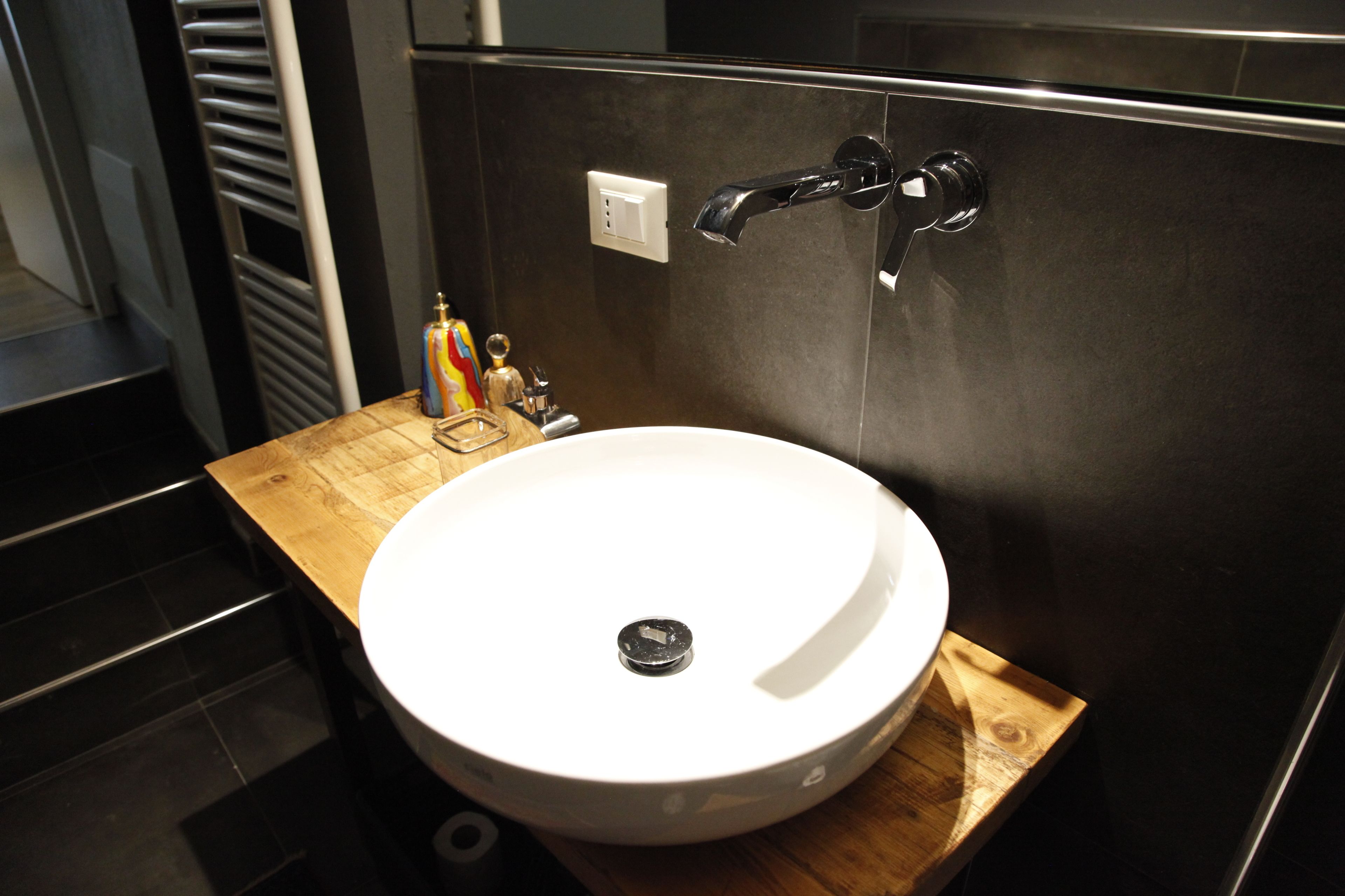 Ein modernes Badezimmer mit einem runden weißen Waschbecken, einer Holztischplatte und einem schwarzen Wasserhahn.