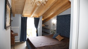 A bedroom with a wooden ceiling, a bed with a patterned bedspread, a dresser, a radiator, and a window with curtains. - Juliet's Nest (Verona)