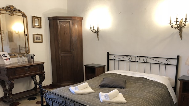 Une chambre d’hôtel bien aménagée, avec un lit, une armoire en bois, un bureau avec un miroir et des lampes fixées au mur.