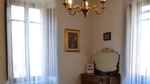Une pièce avec un canapé rouge, une table en bois, une chaise à armature métallique, un lit avec des serviettes, un lustre et une commode en bois.