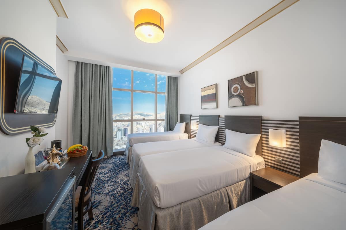 A hotel room with two beds, a large window with a city view, a flat-screen TV, and a dining area with a table and chairs.