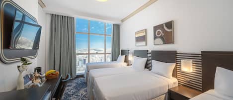 A hotel room with two beds, a large window with a city view, a flat-screen TV, and a dining area with a table and chairs.