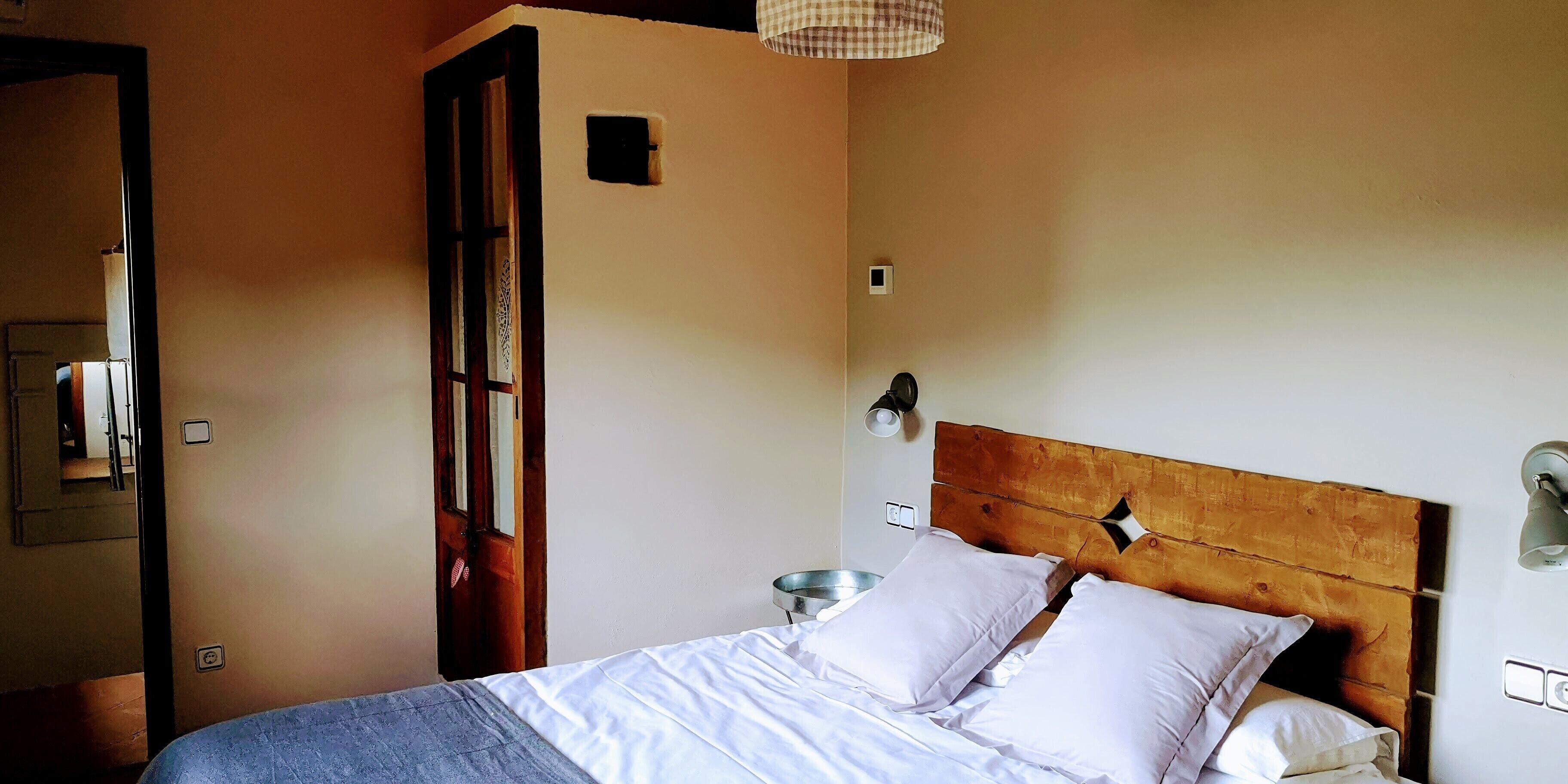 A bedroom with a wooden headboard, a bed with white linens, a nightstand, and a wall-mounted lamp.