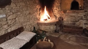 A stone-walled room with a fireplace, a bed with a patterned bedspread, and a bench. - Mas de l'Arlequi Casa rural (Montblanc)