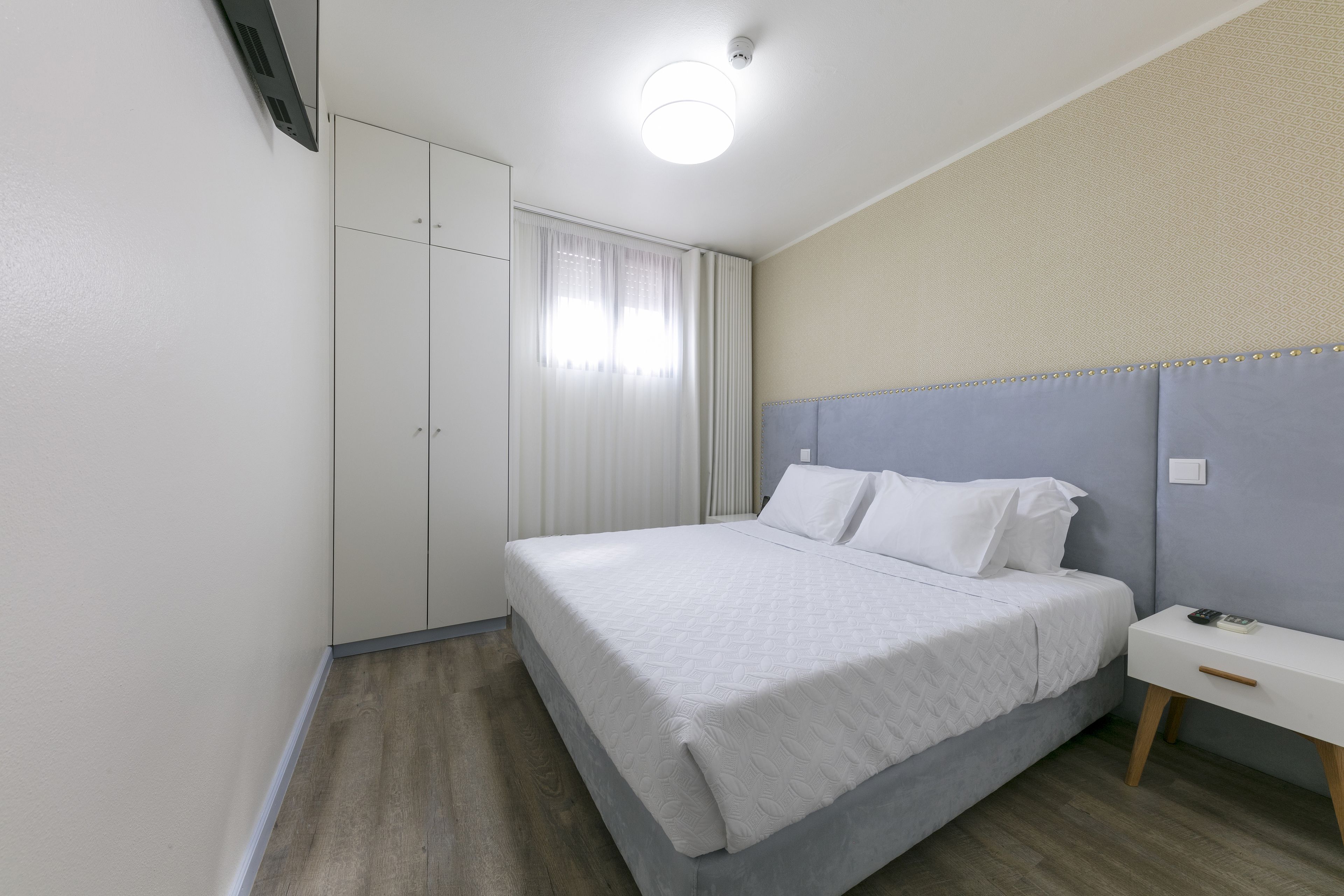 A bedroom with a bed, a bedside table, a wardrobe, and a window with curtains.